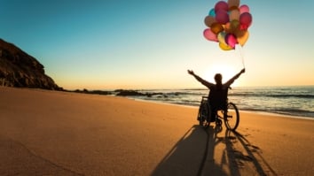Woman in a wheelchair at the beach holding balloons